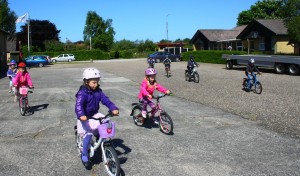 Børnene cykler på pladsen ind og ud mellem hinanden. 